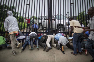 Burundian students slide under the main access gate of the US Embassy compound in Bujumbura on Thursday, seeking refuge after police threatened to break up their camp outside the compound. (AFP PHOTO/MARCO LONGARI)