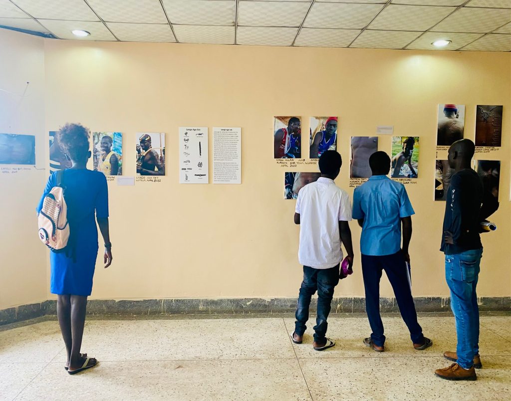 Photograph 1 Visitors to the exhibition ‘Stories on the Body: Murle youth, age-sets and changing body art & scarification in Greater Pibor’, held at the University of Juba in October 2022.